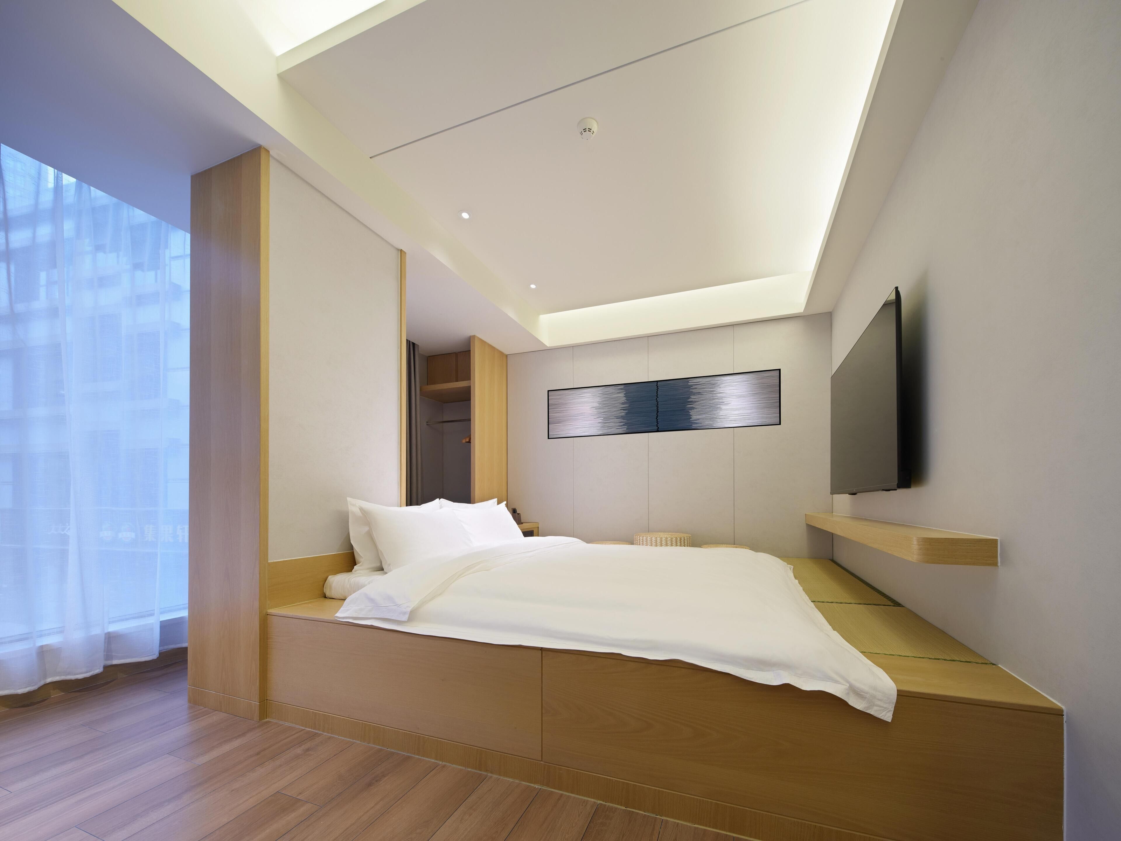 Een moderne slaapkamer met een bed, inbouwkasten, een wandtelevisie en een groot raam.