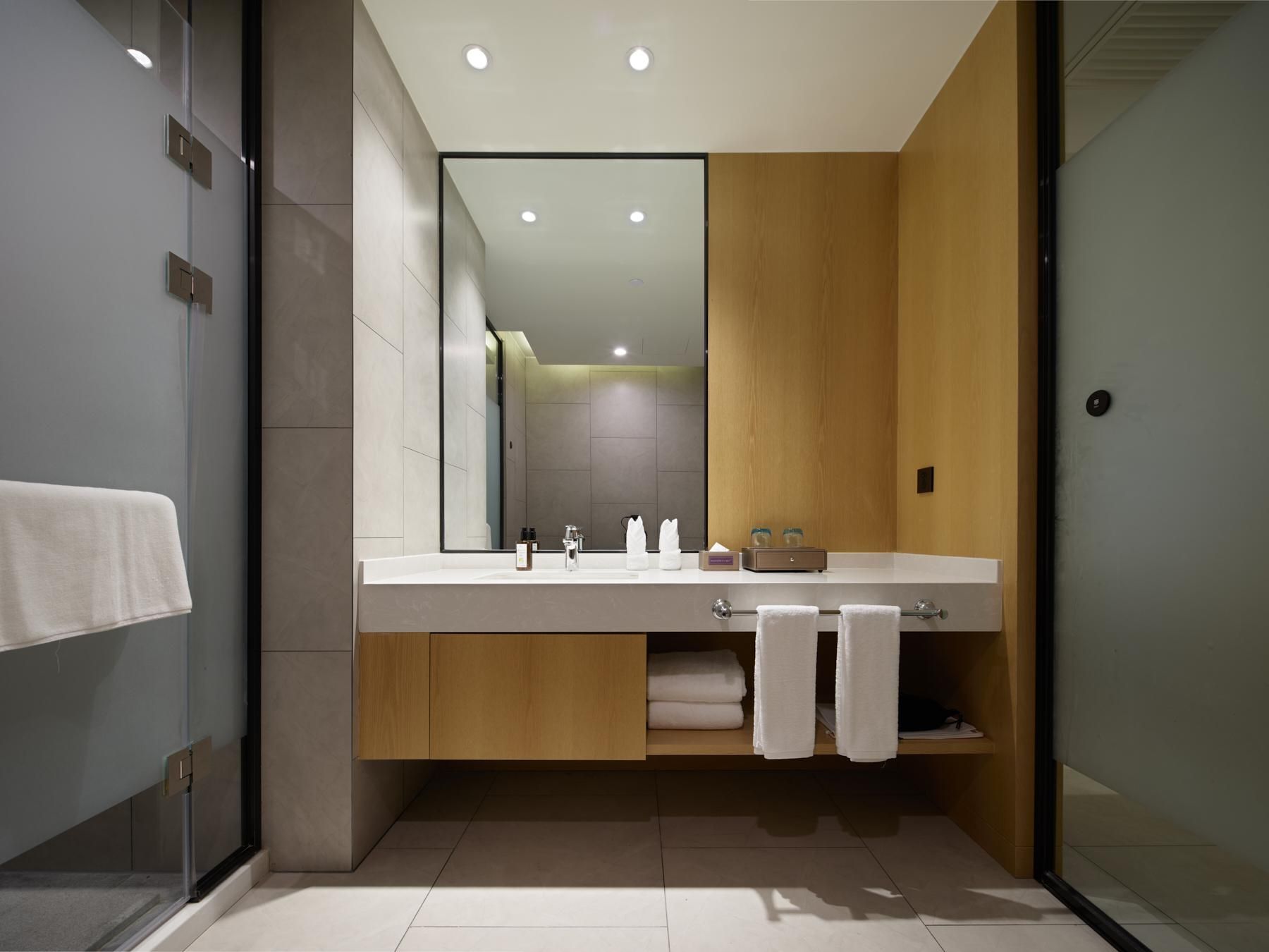 A modern bathroom with a large mirror, a wooden vanity, and a glass shower enclosure.