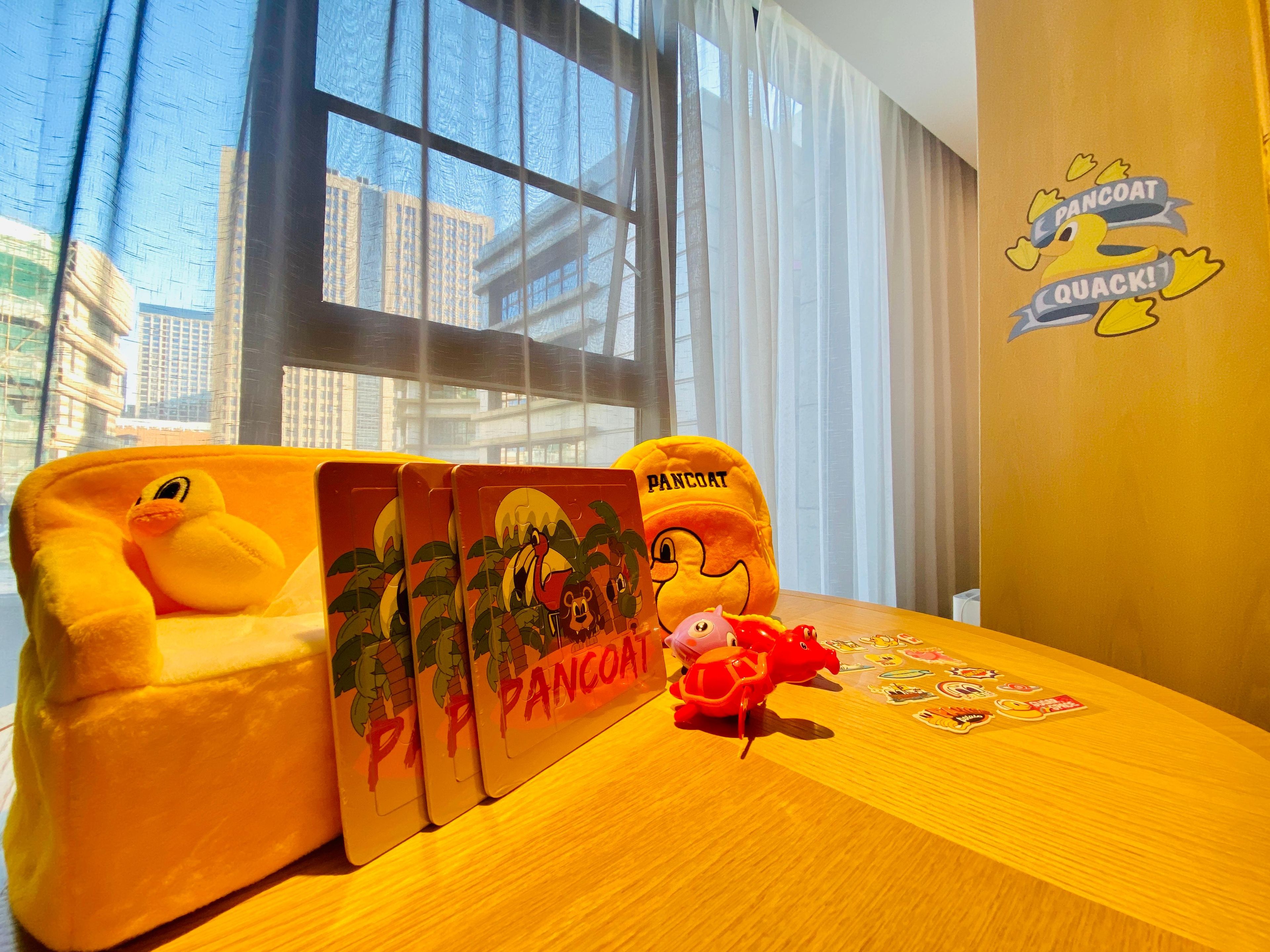 A room with a large window, a plush toy, a small table with a placemat, and a wall sticker.