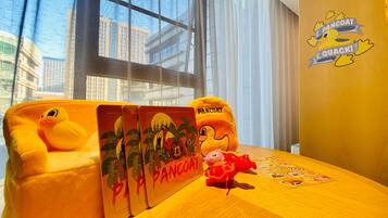 A room with a large window, a plush toy, a small table with a placemat, and a wall sticker.