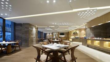 Un comedor moderno con mesas y sillas redondas, una barra de cocina y un ventanal grande.