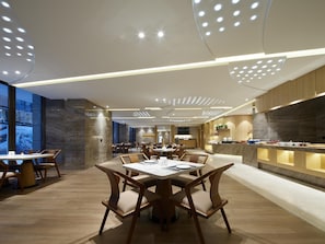 A modern dining area with round tables and chairs, a kitchen counter, and a large window. - Madison Hotel Xianyang Zhuquan Road Wanda Plaza (Xianyang)
