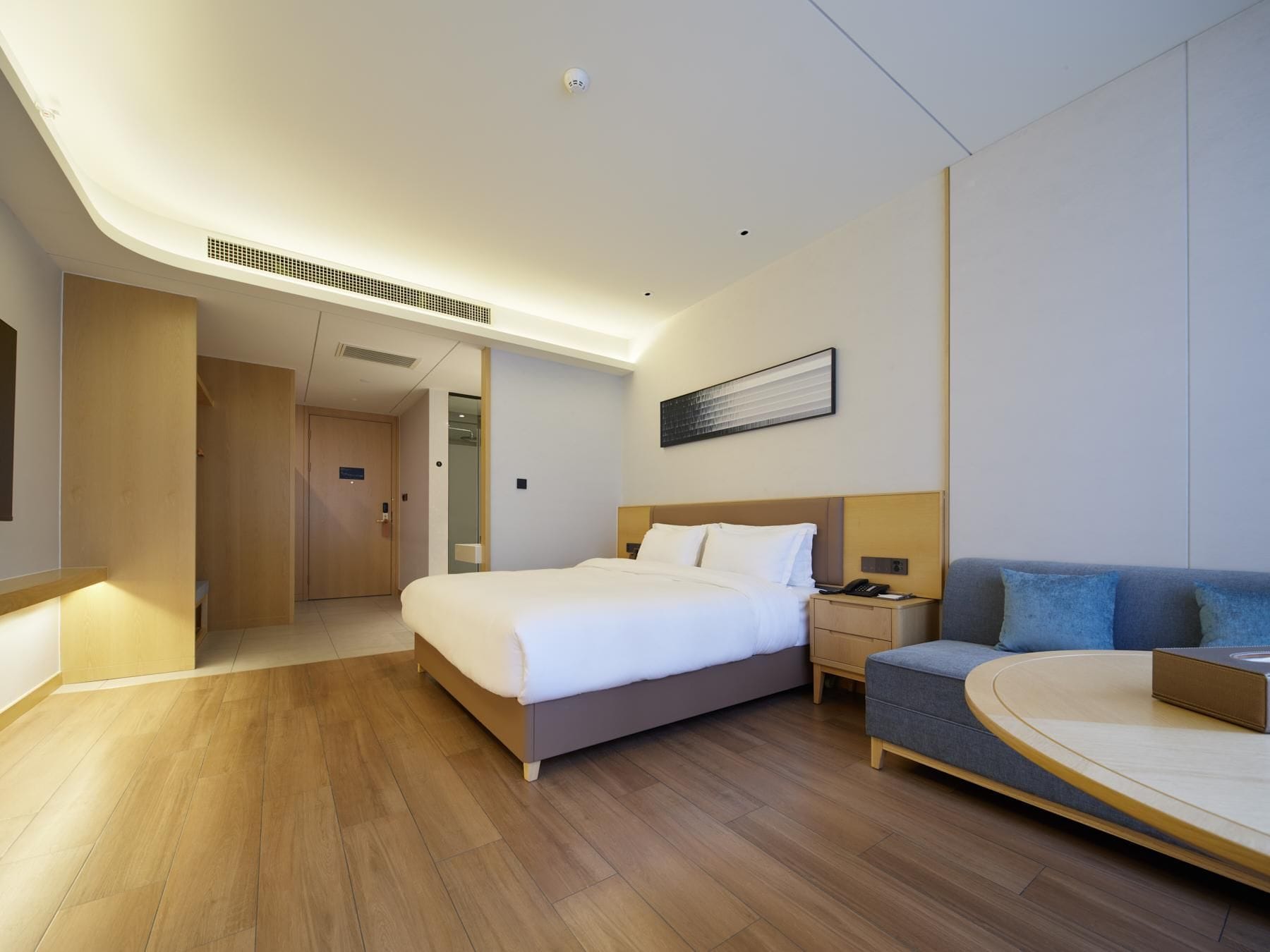 A modern hotel room with a large bed, a bedside table, a sofa, and a round coffee table.