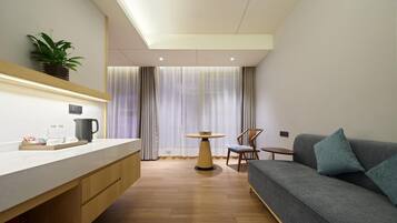 A modern hotel room with a wooden floor, a grey sofa, a small table, and a plant on the wall.