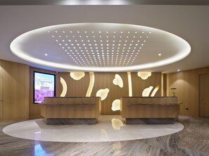 Un espace d’accueil moderne doté de deux comptoirs en marbre, d’un grand écran numérique et d’un plafond orné d’un luminaire original.