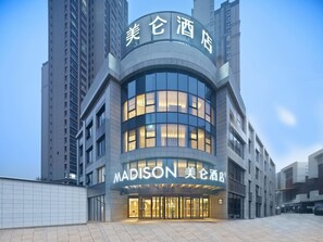 A modern hotel with a curved facade, large glass windows, and a prominent signage. - Madison Hotel Xianyang Zhuquan Road Wanda Plaza (Xianyang)