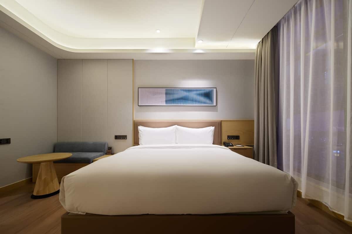 Ein modernes Hotelzimmer mit einem großen Bett, einem Nachttisch, einem Sessel und einem Wandbild.