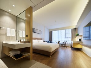 A modern hotel room with a large bed, a bathroom with a vanity, a dining area with a table and chairs, and a large window providing natural light. - Madison Hotel Xianyang Zhuquan Road Wanda Plaza (Xianyang)