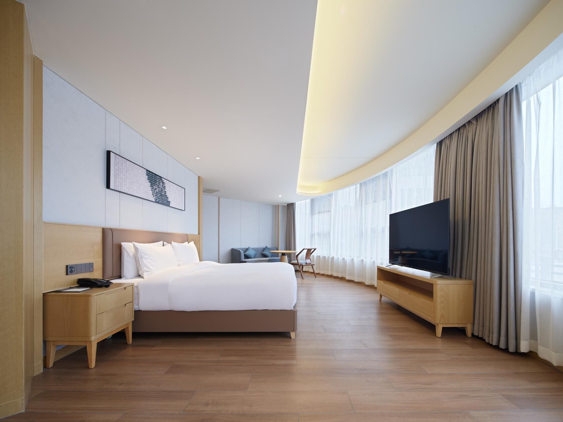 Ein modernes Hotelzimmer mit einem großen Bett, einem Flachbildfernseher, einem Schreibtisch und einer Couch.
