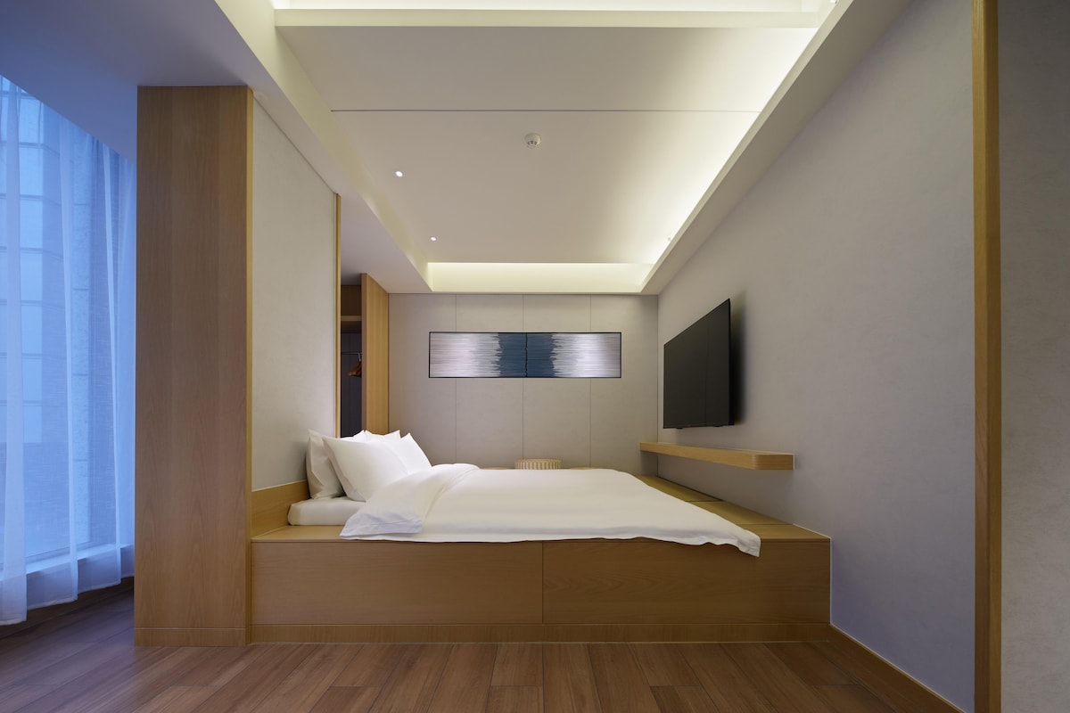A modern bedroom with a built-in bed, a flat-screen TV mounted on the wall, and a skylight above.