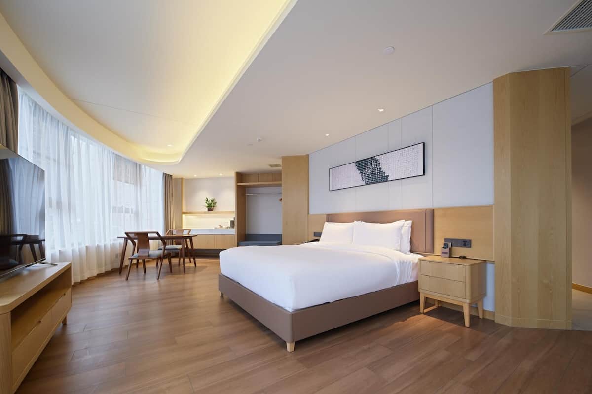 Ein modernes Hotelzimmer mit einem großen Bett, einem Schreibtisch und einem Sessel. In der Ecke befindet sich eine kleine Küchenzeile.