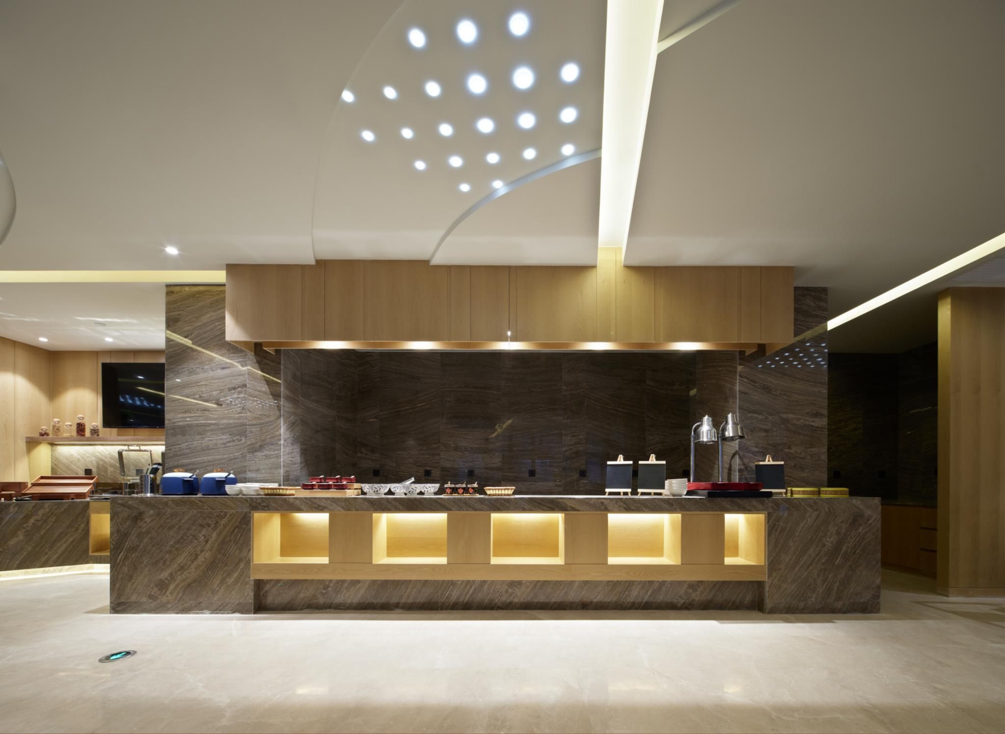 Una moderna reception con piano in marmo, illuminazione integrata e un soffitto ornato da un lampadario geometrico.
