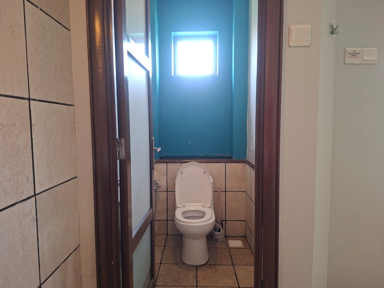 A bathroom with a toilet, a visible light switch, and a door leading to another room.