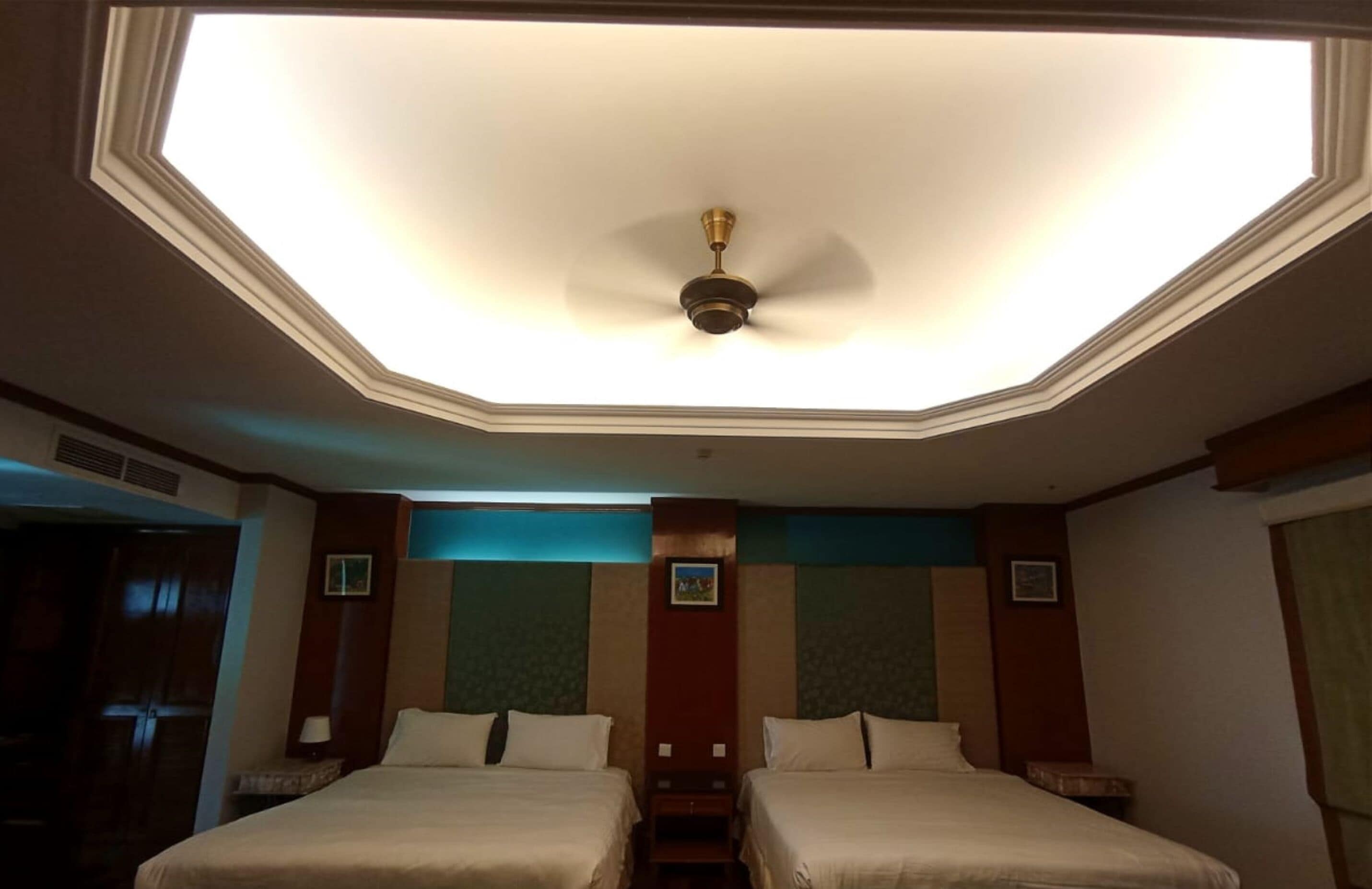 A hotel room with two beds, a ceiling fan, and a skylight.