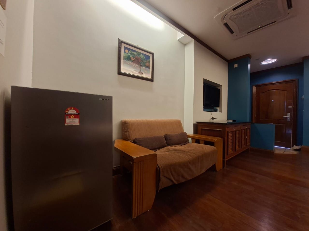 A room with a wooden floor, a sofa, a small table, a refrigerator, and a door.