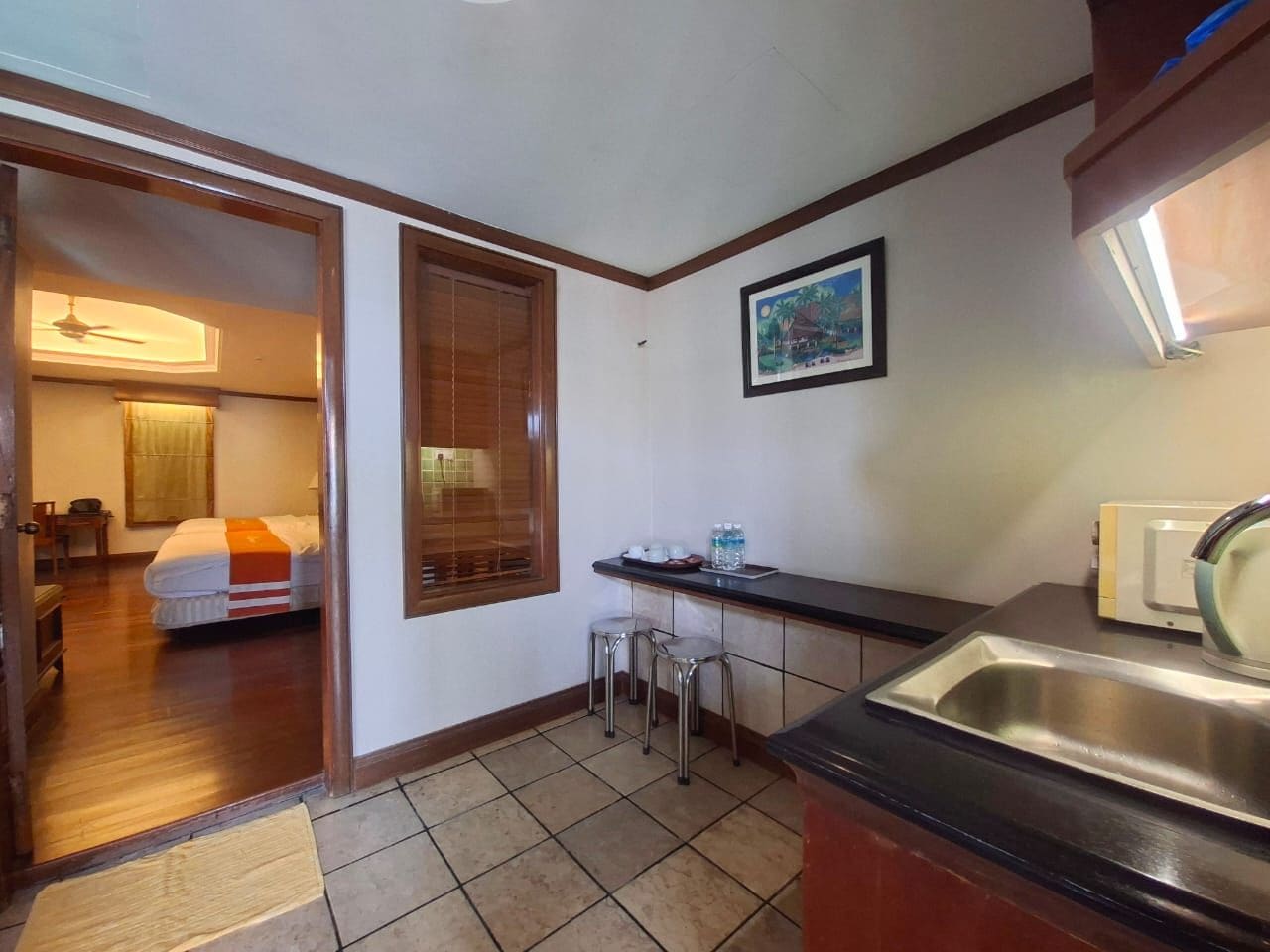 A compact hotel room with a bed, a small kitchenette, a sink, and a window.