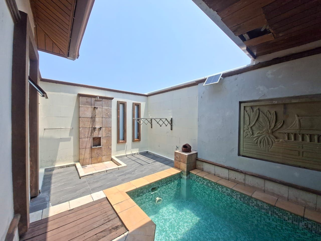 A swimming pool with a tiled deck, a wooden door, and a wall with a decorative relief.