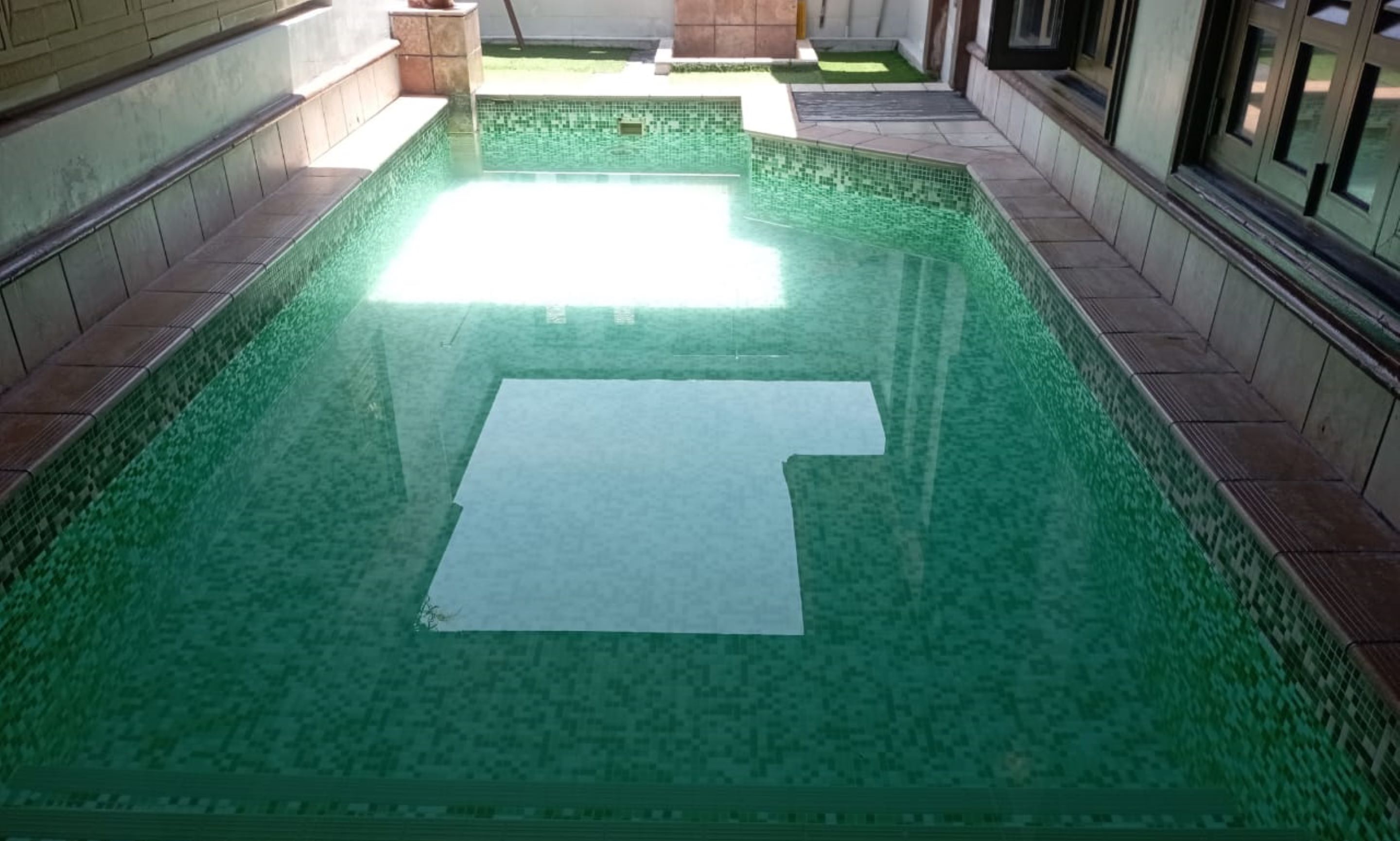 Una piscina con borde de azulejos y un objeto rectangular blanco en el centro.