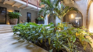 A spacious indoor courtyard with a central palm tree, surrounded by various plants and a stone staircase leading to an upper level. - Cinco Quintas Hotel Boutique (Cartagena)