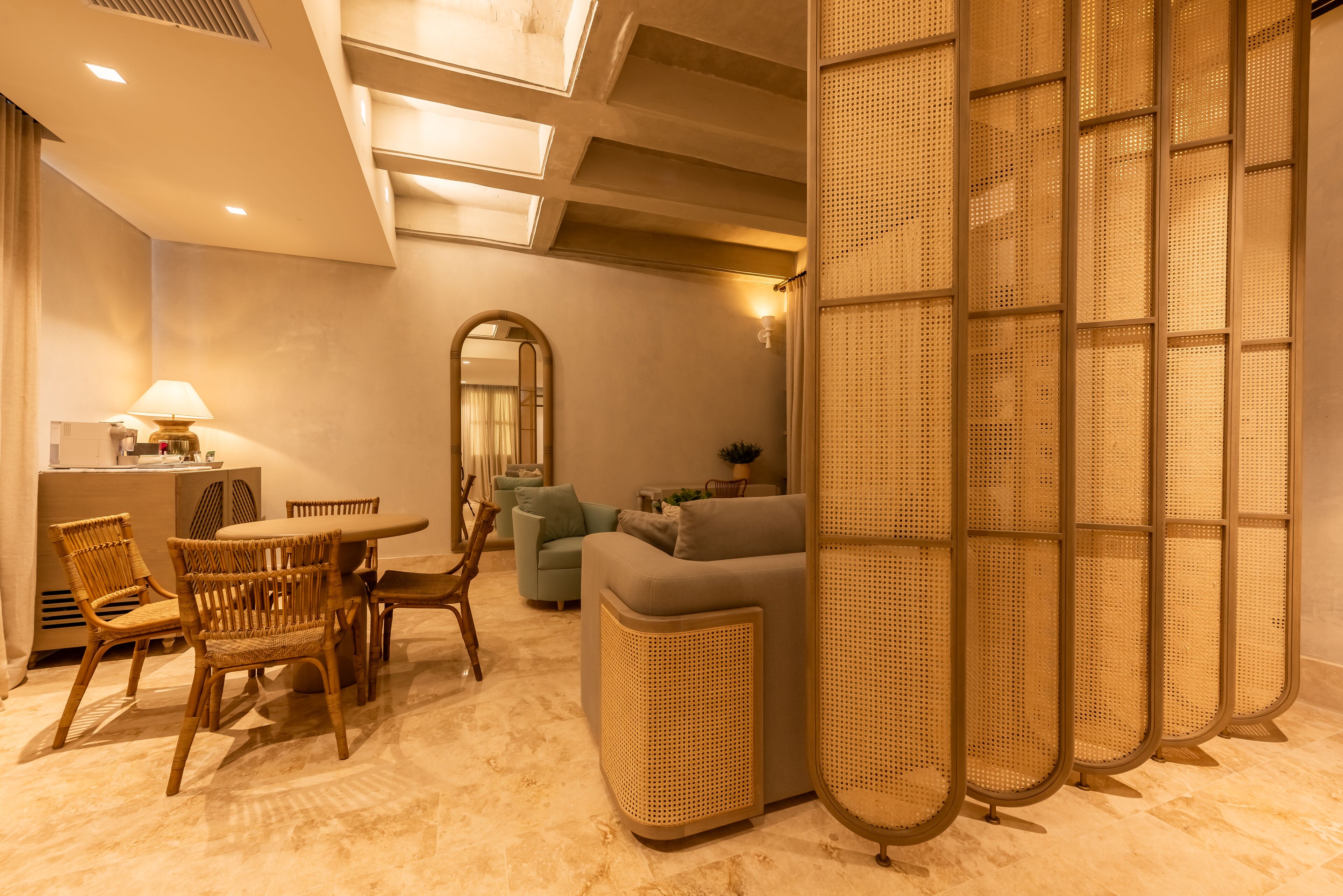 A modern hotel room with a dining area, a sofa, and a large mirror.