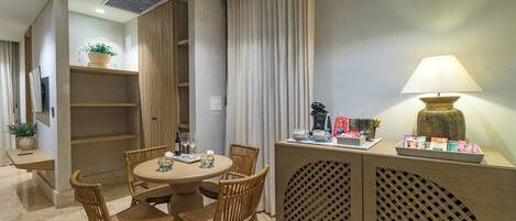 A dining area with a round table, wicker chairs, a cabinet with a lamp, and a potted plant.