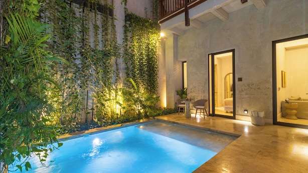 A swimming pool with a tiled deck, surrounded by lush greenery and a building with a balcony. - Cinco Quintas Hotel Boutique (Cartagena)