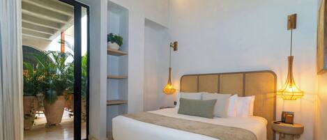 A bedroom with a bed, bedside tables, a potted plant, and a view through a glass door.