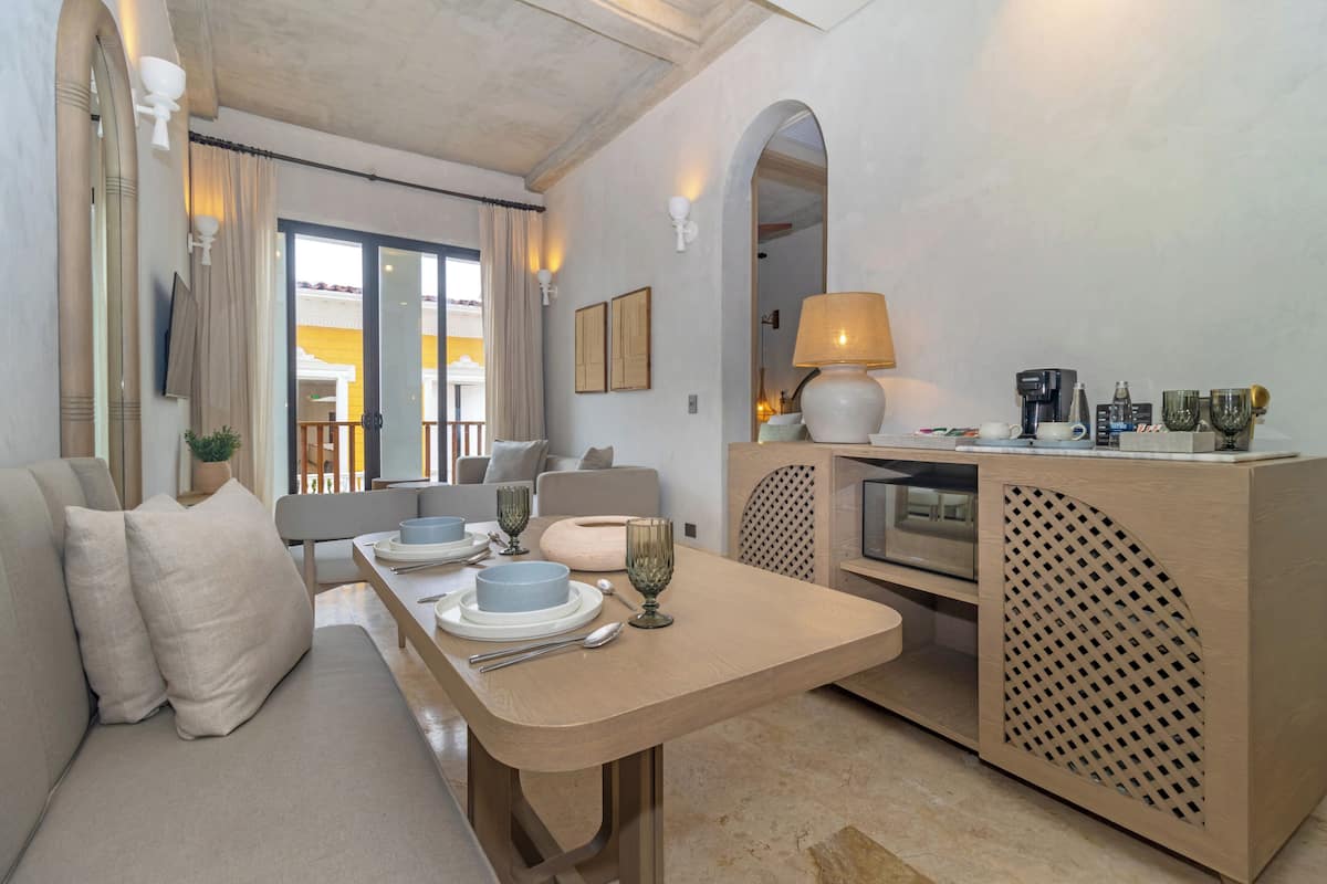 A modern living room with a sofa, dining table, and a kitchen area with a coffee machine.