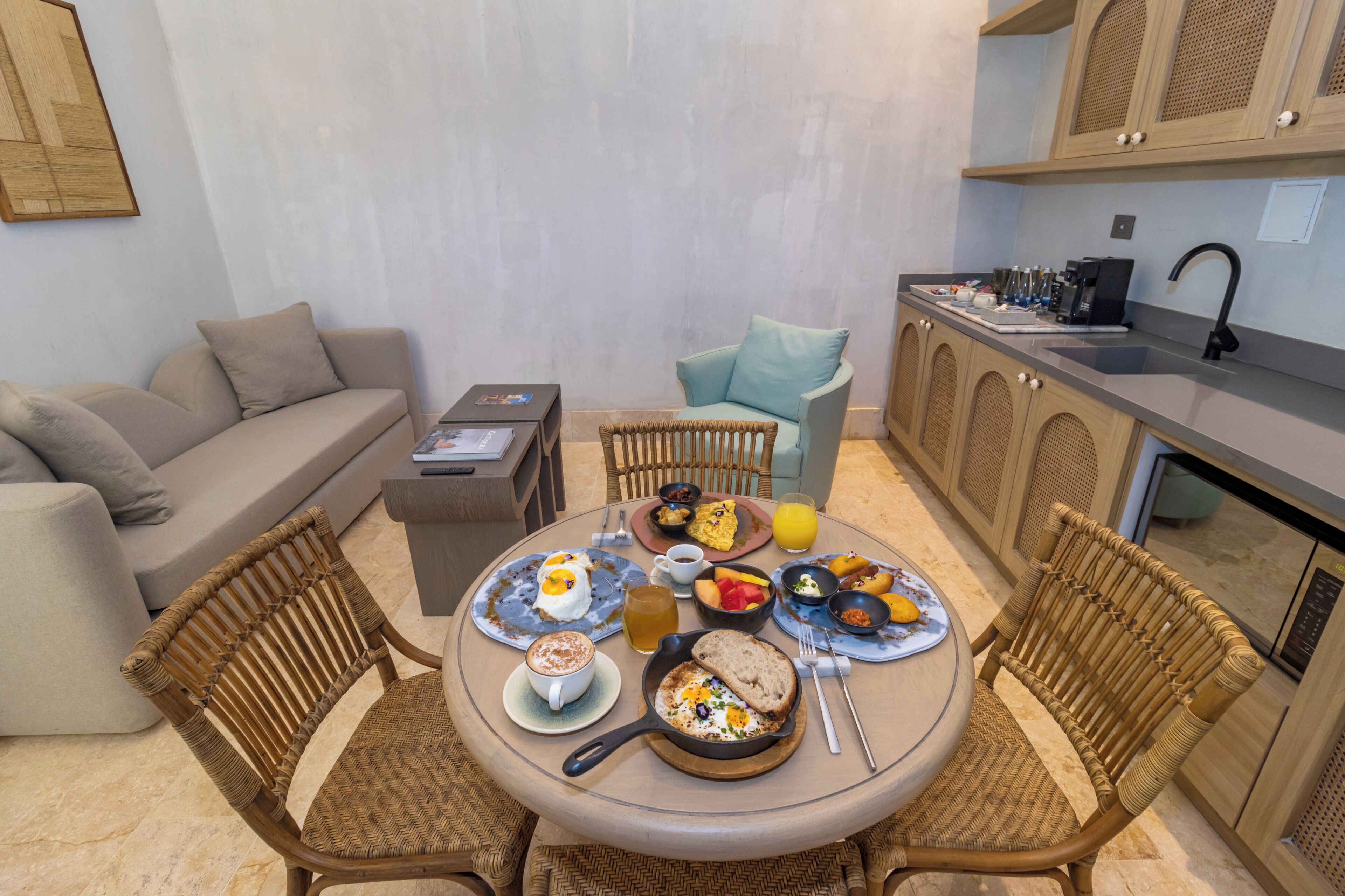 A breakfast setup with wicker chairs, a round table, and a kitchenette in the background.