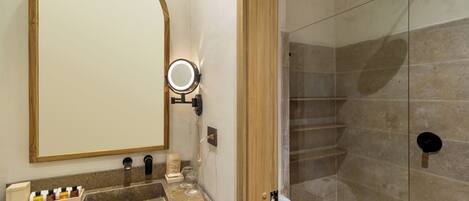 A bathroom with a vanity, a mirror, a shower, and a glass-enclosed shower stall.