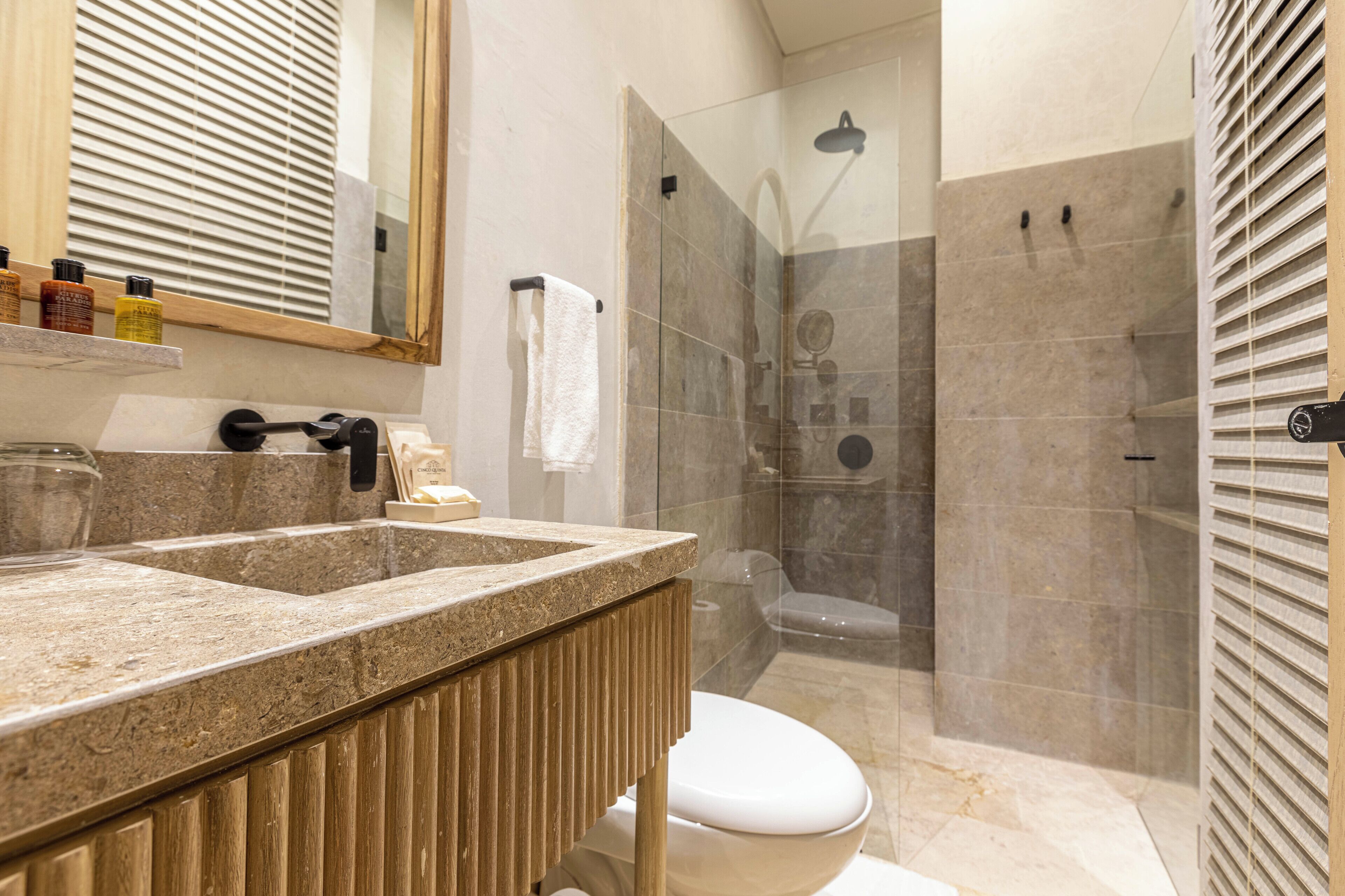 A bathroom with a large mirror, a sink with a wooden vanity, a toilet, and a glass-enclosed shower area.