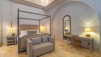 A bedroom with a four-poster bed, a sofa, a desk with a chair, and a mirror.