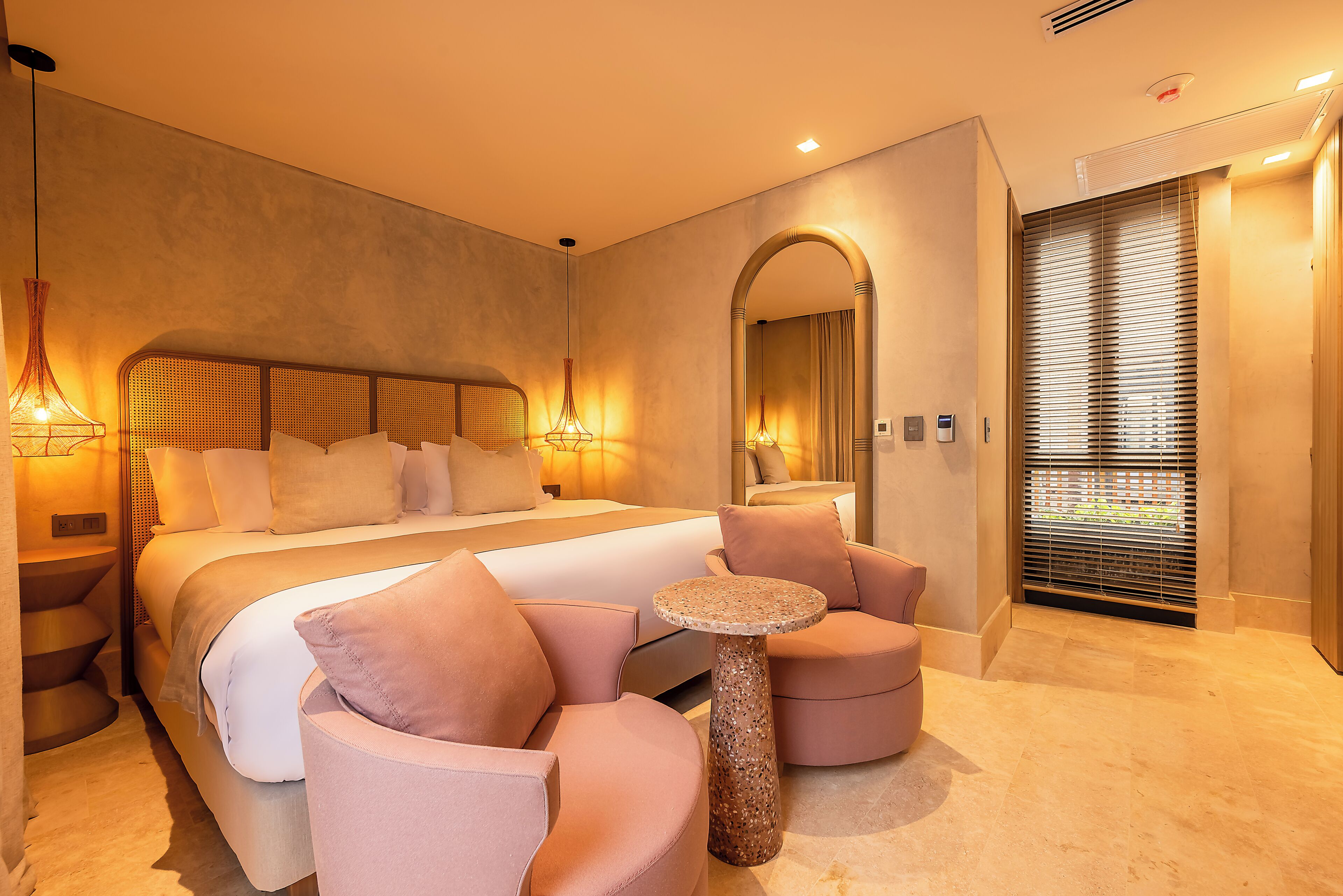 A modern hotel room with a large bed, two seating areas, a small table, and a large mirror.
