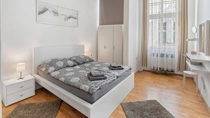 Un dormitorio moderno con cama, mesitas de noche, armario, escritorio con espejo y ventana con cortinas.