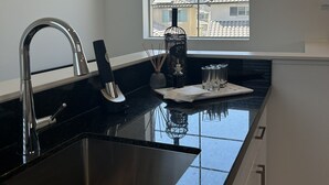 A modern kitchen with a stainless steel sink, a window with a mountain view, and a black countertop. - PGA WEST Whisper Rock #254648 (La Quinta)