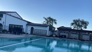 A swimming pool with a clear blue water, surrounded by a white building with a tiled roof and a stone wall. - PGA WEST Whisper Rock #254648 (La Quinta)