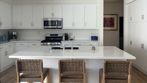 A modern kitchen with white cabinetry, a central island with bar stools, stainless steel appliances, and recessed ceiling lights. - PGA WEST Whisper Rock #254648 (La Quinta)