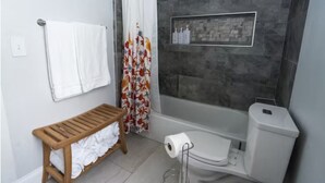 A bathroom with a shower, toilet, and a bench with towels.