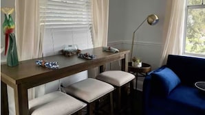 A room with a wooden table, two cushioned benches, a blue sofa, a floor lamp, and a window with blinds.