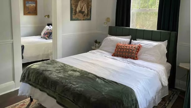 A bedroom with a bed, a nightstand, a mirror, and a window with curtains.