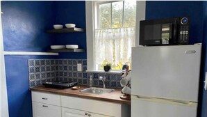 A compact kitchen with blue walls, a white refrigerator, a microwave, a sink, and a window with a view of greenery.