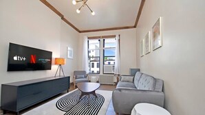A modern living room with a flat-screen TV displaying Apple TV, Netflix, and Prime Video logos, a grey sofa, a white coffee table, and a black and white striped rug. - Centralized apt in Park Slope near the park and the city (Brooklyn)