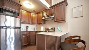 A kitchen with wooden cabinets, stainless steel appliances, a white countertop, and two wooden chairs. - Centralized apt in Park Slope near the park and the city (Brooklyn)