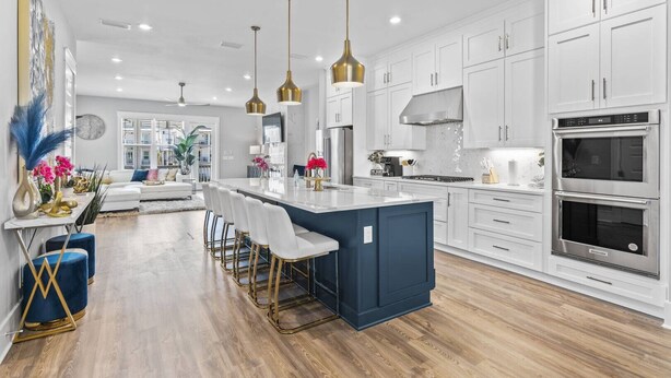 A modern kitchen with white cabinets, a central island with bar stools, stainless steel appliances, and pendant lighting.
