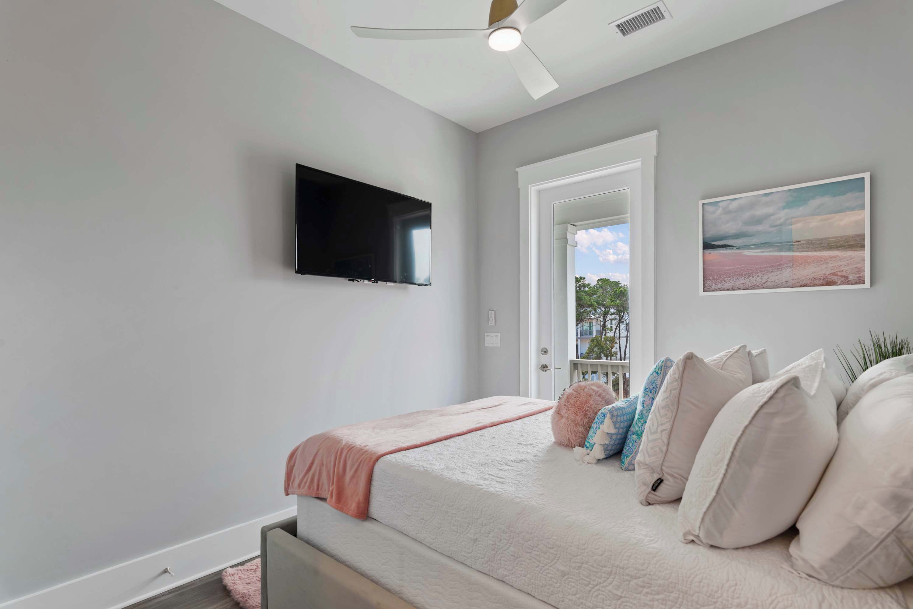 A bedroom with a bed, a ceiling fan, a TV mounted on the wall, and a window with a view.