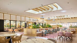 A spacious hotel lobby with a central seating area, multiple dining tables, and a variety of seating options including sofas and chairs.
