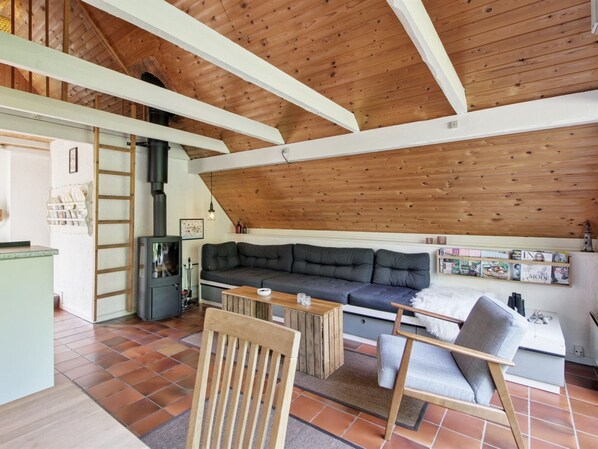 A cozy loft-style living space with a sloped ceiling, a built-in sofa, a wooden coffee table, and a fireplace.