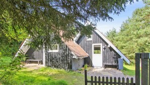Een rustieke houten hut met een schuin dak, een klein terras en een omheinde tuin.