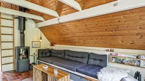 Een gezellige woonkamer met een houten plafond, een grijze bank, een houten salontafel en een open haard.