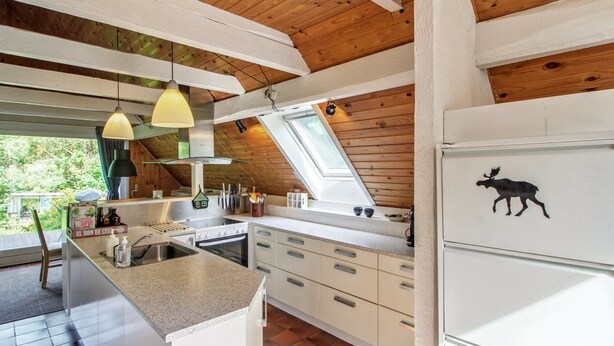 Een moderne keuken met een centraal eiland, houten balken in het plafond en een raam met uitzicht op groen.